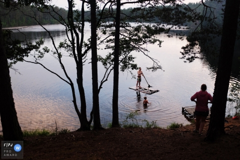 A man stands on a raft while his son stands in the water as his mother watches in this image created by a Saint Petersburg, Russia family photographer.