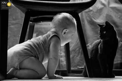 An Antwerp, Belgium documentary family photographer captured this toddler playing with a black cat under the table