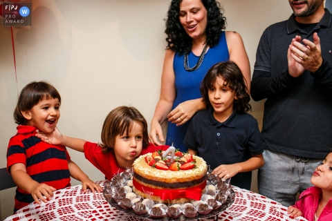 Photographie de famille documentaire de Belo Horizonte montrant le garçon pousse son petit frère pour qu'il ne puisse pas souffler sa bougie d'anniversaire dans une scène hilarante