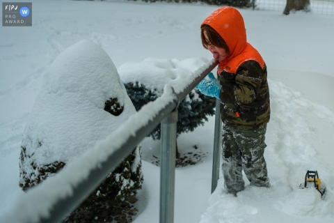 A Phoenix documentary family photographer captured this Little boy as he makes his way up a walkway, licking snow from a handrail