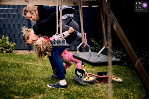 Familiefotografie in Bonn die de kus bij de speelplaats vastlegt terwijl ze op de rug van mama rijdt