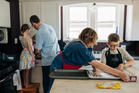 père et fille travaillent au comptoir de la cuisine avec dos à la caméra tandis que la mère et le fils déroulent du papier parchemin sur l'îlot de cuisine.