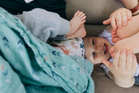 preschool girl examines toes while newborn sibling's toes right above her