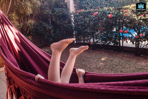 In São Paulo, Brazil, a child plays joyfully in a hammock on the porch, their feet playfully swinging overhead in the sunlight, capturing the carefree spirit of childhood in the backyard.