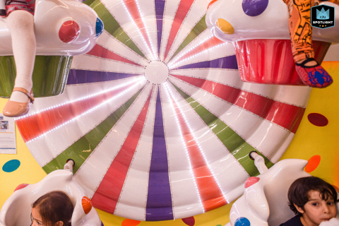 In São Paulo, Brazil, a documentary-style family picture captures children enjoying a Wheel of Fortune ride at a lively kids' party, highlighting the fun and excitement of the occasion.