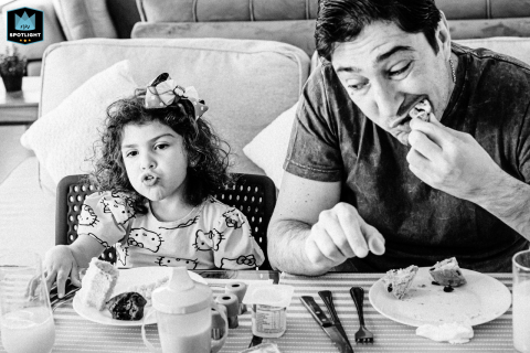 In São Paulo, Brazil, a black-and-white photo captures a dad and daughter at the breakfast table, both with expressive faces, showcasing the joy and connection of their morning together.