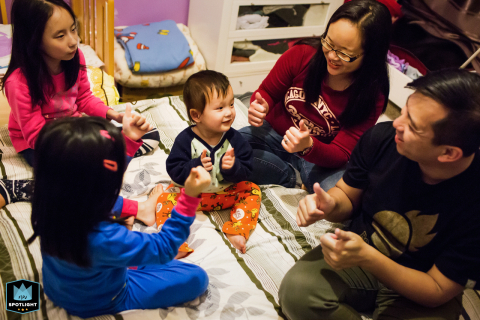In San Francisco, California, a family gathers on the ground around a toddler for game time at home, highlighting their closeness and shared joy in playful activity.