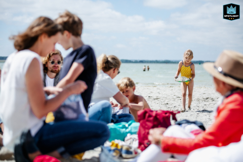 In Houston, Texas, as the family relaxes on towels and blankets at the beach, a determined little girl hauls handfuls of sand, embodying joyful persistence.