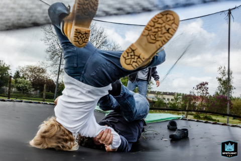 Dynamic playtime in Houston, Texas: Dad joyfully tosses his sons on the backyard trampoline, their laughter echoing under a cloudy outdoor sky.