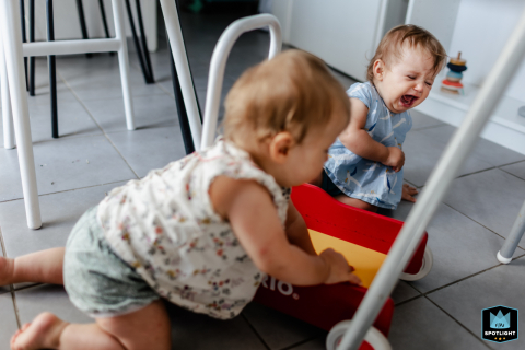Twin rivalry in Houston, Texas: one sibling snatches a toy on the dining room floor tiles, resulting in quick tears and heartfelt childhood drama.