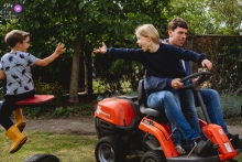 NL - Photos de famille en plein air dans la cour arrière d'une séance photo à domicile montrant le travail avec papa tout en jouant avec son frère