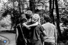 Schwarzweiss-NL-Familienfotografie von einer Naturwanderung in Gelderland, während sie um den Hals des Vaters hängen