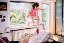 A Bonn little girl jumping on a bed where her father is lying at home in North Rhine-Westphalia