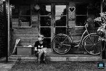 In North Yorkshire, England, a boy sits quietly on the garden shed steps with his lunch plate. A bike rests on the porch, evoking vintage black-and-white nostalgia.