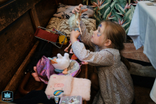 In North Yorkshire, England, a girl with face paint sits at the dinner table, happily playing with her toys on a bench, lost in imaginative play.