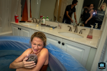 In Ventura, California, mom gazes lovingly at her newborn, completely absorbed, while her husband and the birth team stand nearby, discussing the next steps together.