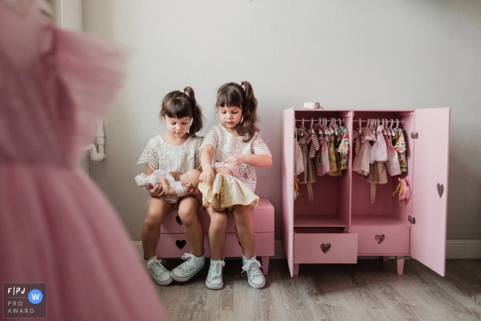 Two identically dressed girls play with dolls in their room in this photo captured by a Saint-Petersburg family documentary photographer.