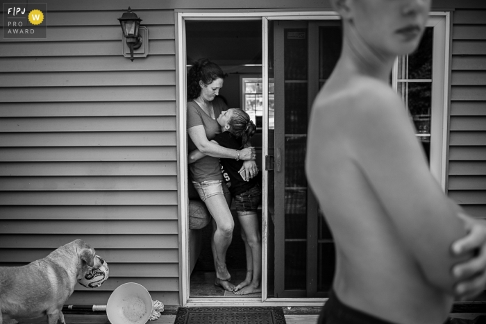 Le photojournaliste de la famille de Brooklyn a capturé cette photo en noir et blanc d'une mère et d'une fille s'embrassant dans l'embrasure de la porte pendant que le chien de la famille attend que quelqu'un lui lance une balle