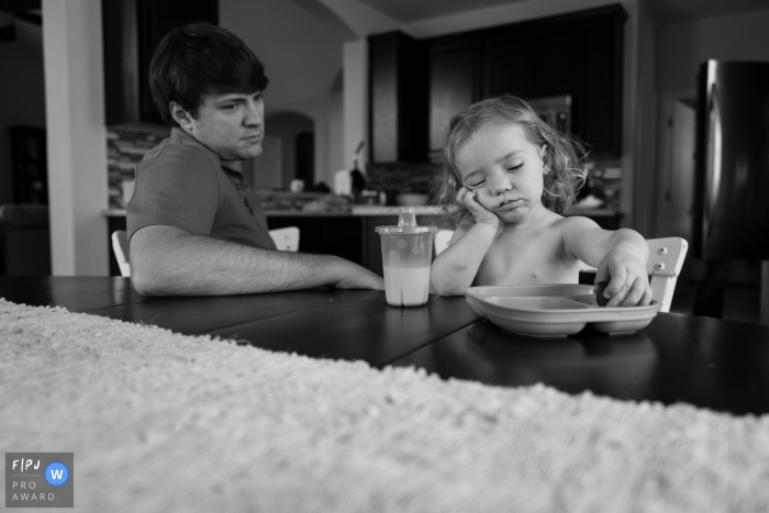 Photo by: <a href="https://www.fpja.com/documentary-family-photography-contests/benjamin-lipford/atlanta/2035341">Benjamin Lipford - United States</a> A toddler who is bored with lunch while dad waits nearby was captured at their kitchen table by an Atlanta Georgia documentary family photographer