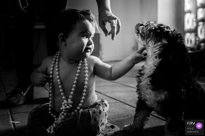 A little girl wears a large pearl necklace while she pets her dog in this image created by a Landes family photographer.