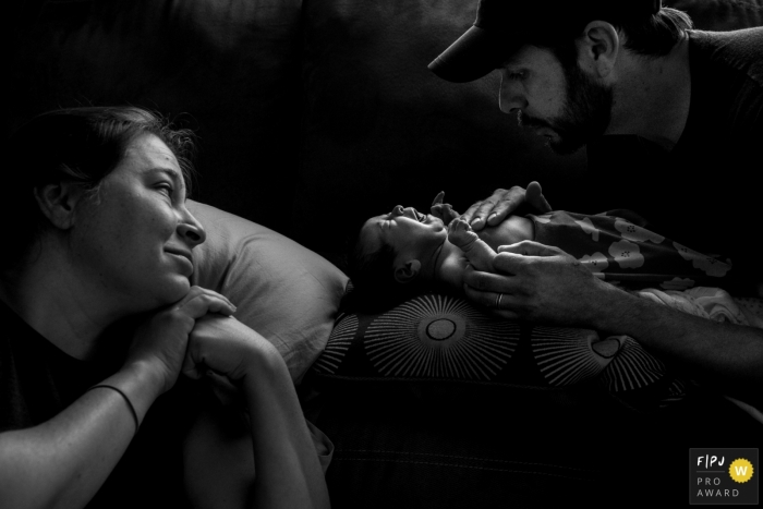 Une femme regarde pendant que son mari tente de calmer leur bébé en pleurs sur le canapé, sur cette photo prise par un photographe de famille primé à Boulder, CO.