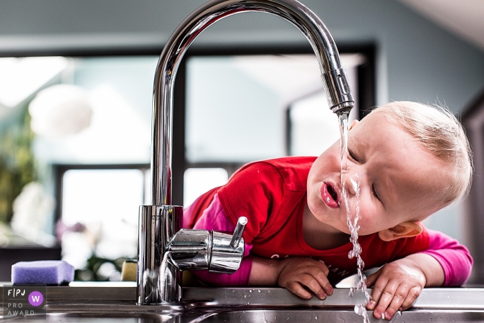 Photo by: <a href="https://www.fpja.com/documentary-family-photography-contests/joshua-dhondt/antwerpen/2060401">Joshua Dhondt - Belgium</a> A little boy tries to drink from the kitchen faucet in this FPJA award-winning picture by an Antwerpen family photographer.