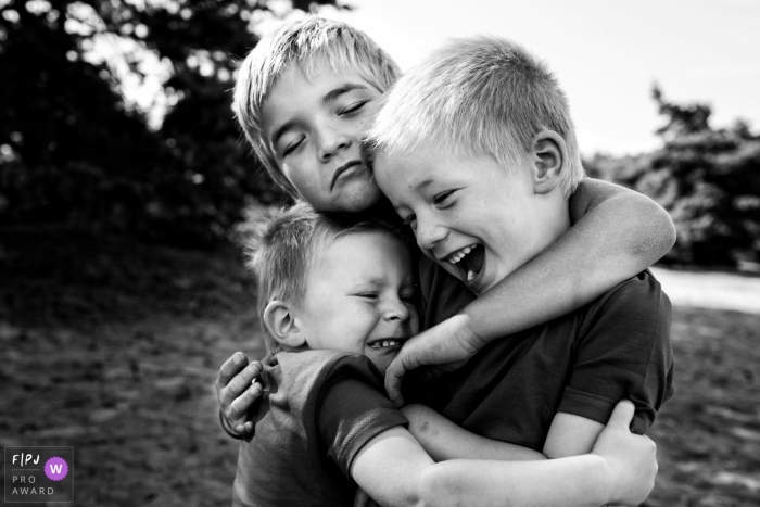 Photo by: <a href="https://www.fpja.com/documentary-family-photography-contests/joshua-dhondt/antwerpen/2060421">Joshua Dhondt - Belgium</a> Three brothers hug each other outside in this documentary-style family photo captured by an Antwerpen photographer.