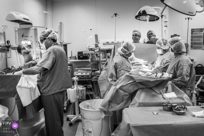 Photo by: <a href="https://www.fpja.com/documentary-family-photography-contests/clara-sampaio/rio-de-janeiro/2060491">Clara Sampaio - Brazil</a> A doctor cleans up a newborn as nurses close the mother's C-section in this black and white photo by a Rio de Janeiro documentary birth photographer.