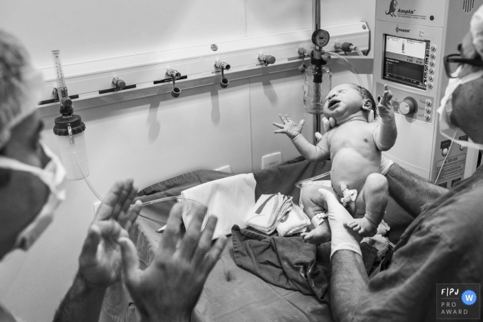 A doctor lifts a newborn up from the hospital table in this black and white birth photo taken by a Rio de Janeiro, Brazil photographer.