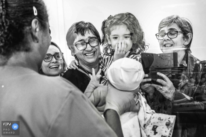 A nurse holds up a newborn baby for its family to see in the hospital in this black and white photo by a Rio de Janeiro, Brazil documentary birth photographer.