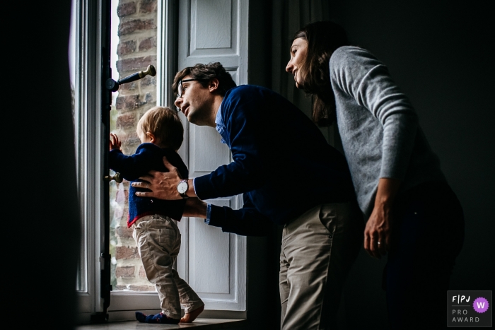 A mother and father help their son look out the window in this family picture by a Brabant Wallon photographer. 