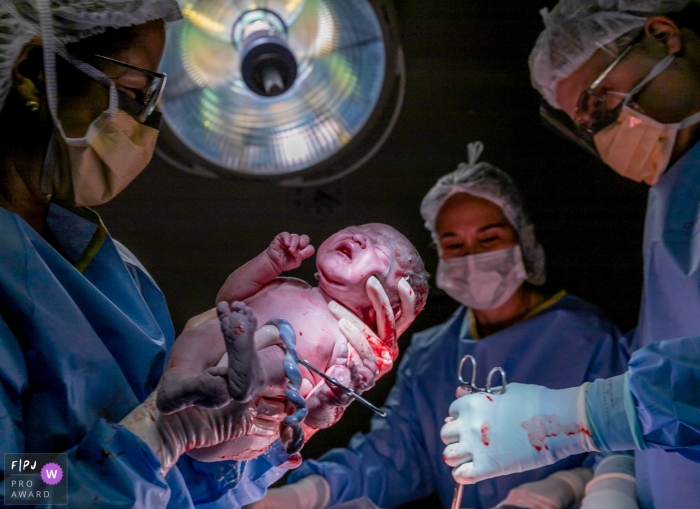 Photo by: <a href="https://www.fpja.com/documentary-family-photography-contests/renata-casali/salvador/2061386">Renata Casali - Brazil</a> A doctor holds a newborn and prepares to cut the umbilical cord in this image recorded by a documentary-style Salvador birth photographer.