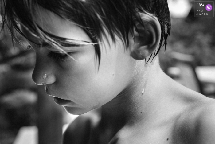 Photo en noir et blanc d'un garçon qui vient de sortir d'une piscine, enregistrée par un photographe de famille de style documentaire primé à Paris, en France.