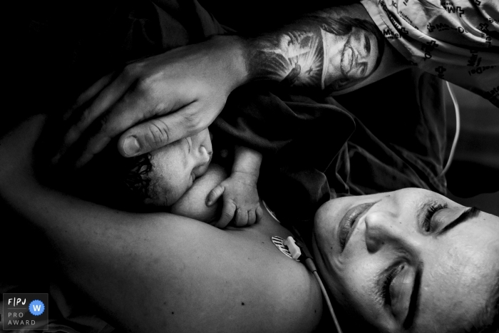 Photo by: <a href="https://www.fpja.com/documentary-family-photography-contests/eduardo-bedran/minas-gerais/2062301">Eduardo Bedran - Brazil</a> A father and mother hold their newborn on the hospital bed in this black and white award-winning photo captured by a Minas Gerais, Brazil birth photographer.