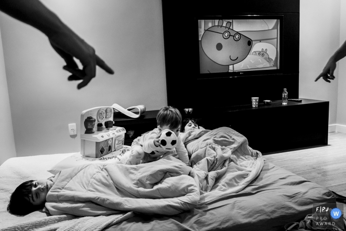Photo by: <a href="https://www.fpja.com/documentary-family-photography-contests/eduardo-bedran/minas-gerais/2062321">Eduardo Bedran - Brazil</a> A boy lays in bed as his brother crawls over him with a plush soccer ball in this documentary-style family photo captured by a Minas Gerais, Brazil photographer.