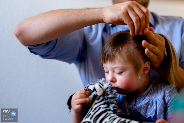 Photo by: <a href="https://www.fpja.com/documentary-family-photography-contests/jess-haverkamp/berlin/2062471">Jess Haverkamp - Germany</a> A little girl kisses her stuffed zebra while her father does her hair in this Family Photojournalist Association awarded photo by a Berlin, Germany documentary family photographer.