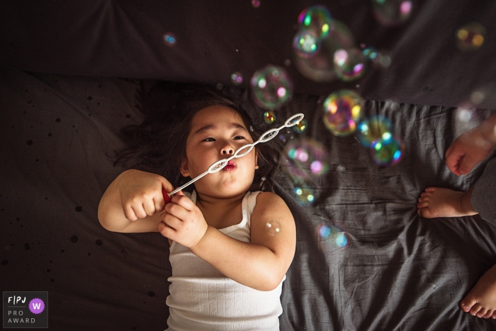 Une petite fille souffle des bulles alors qu'elle se couche au lit dans cette image primée du FPJA, capturée par un photographe de famille de Shanghai, en Chine.