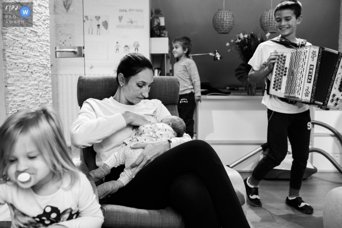 Un garçon joue de l'accordéon pendant que sa mère donne le sein à son petit frère sur cette photo enregistrée par un photographe de famille de style documentaire primé à Ljubljana.