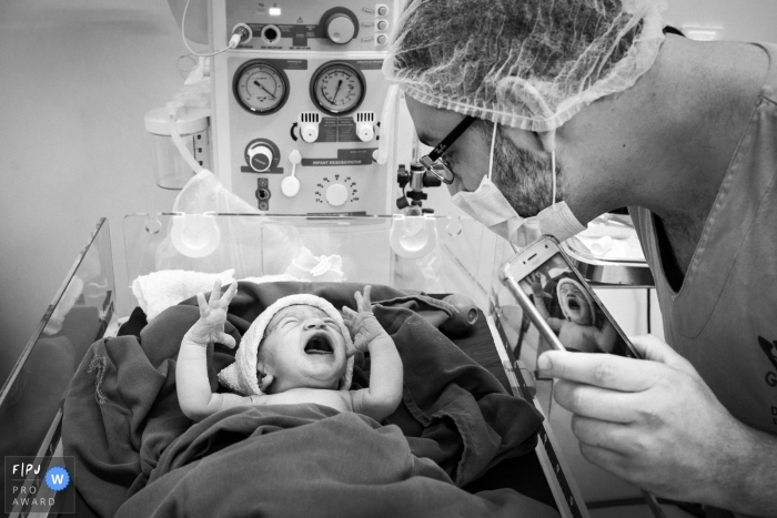 Un père prend une photo de son nouveau-né en pleurs à l'hôpital dans cette photo de naissance en noir et blanc réalisée par un photographe primé du Minas Gerais, au Brésil.