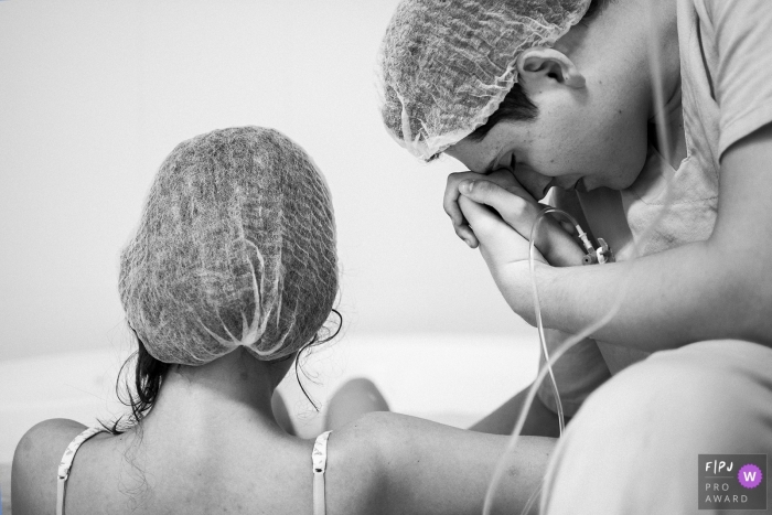 A husband holds his wife's hand in the hospital as she prepares to give birth in this black and white photo composed by an award-winning Minas Gerais, Brazil birth photographer.