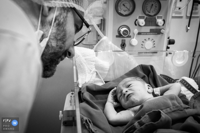 Un père rend visite à son nouveau-né à l'hôpital dans cette image en noir et blanc capturée par un photographe de naissance de style documentaire, Minas Gerais.