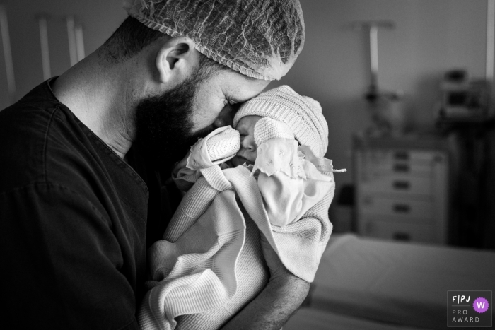 Un père tient son bébé à l'hôpital dans cette image en noir et blanc composée par un photographe de naissance de style documentaire, Minas Gerais.