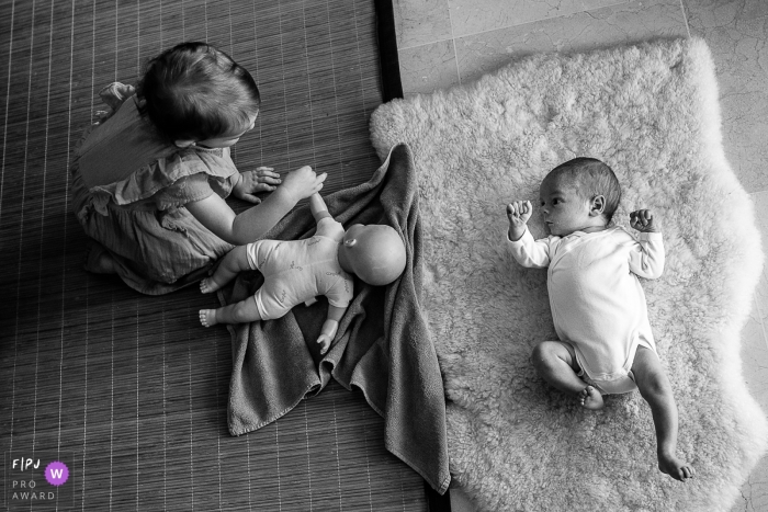 A baby watches his sister play with a baby doll in this documentary-style family photo captured by a Savoie photographer. 