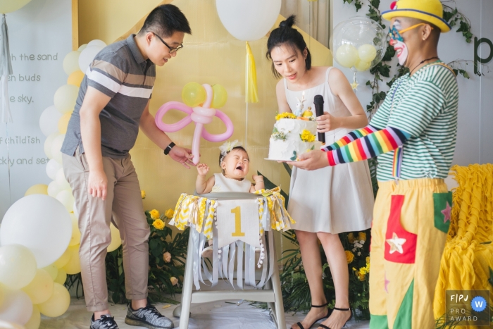Photo by: <a href="https://www.fpja.com/documentary-family-photography-contests/mengjing-yao/zhejiang/2064511">Mengjing Yao - China</a> A baby girl cries at her first birthday when she sees a clown carrying the cake in this photo recorded by a Zhejiang, China award-winning, documentary-style family photographer.