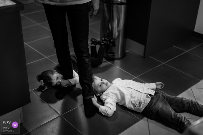 Two children lay on the ground holding onto their parent's legs in this photograph created by a Haute-Garonne family photojournalist. 