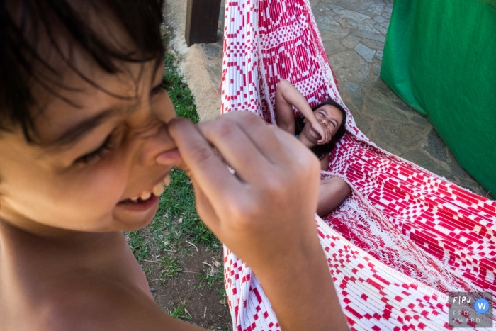 A boy holds his nose as his sister lays laughing in a hammock in this photograph by a Minas Gerais documentary family photographer. 