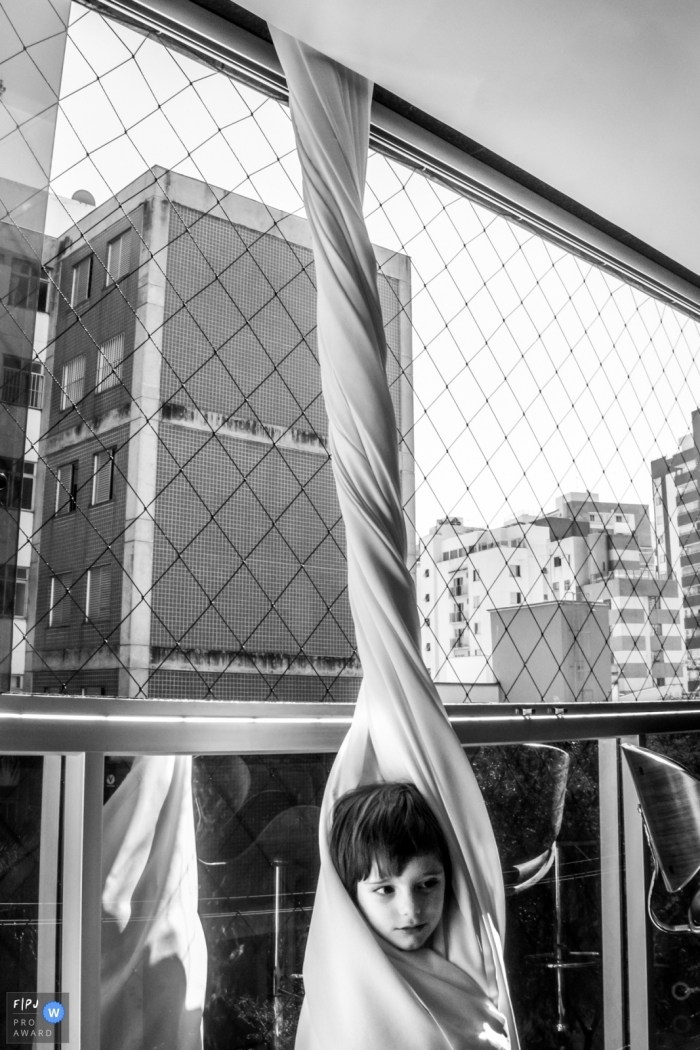 A little boy has wrapped himself in a curtain in this Family Photojournalist Association awarded photo by a Minas Gerais documentary family photographer.