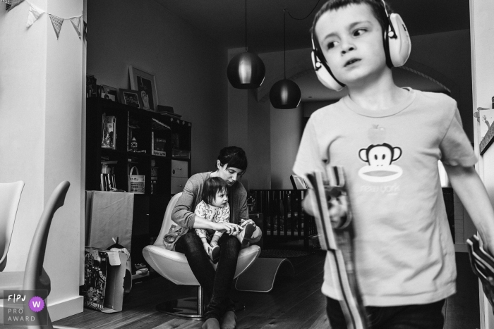 Photo by: <a href="https://www.fpja.com/documentary-family-photography-contests/christophe-de-mulder/antwerpen/2065191">Christophe De Mulder - Belgium</a> A mother helps her daughter put her shoes on as her son walks in front of them wearing earmuffs in this picture captured by an Antwerpen family photojournalist.