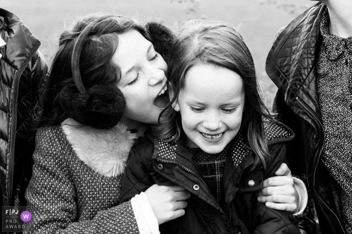 A girl holds her sister as they sit outside between their parents in this photograph created by a London, England family photojournalist. 