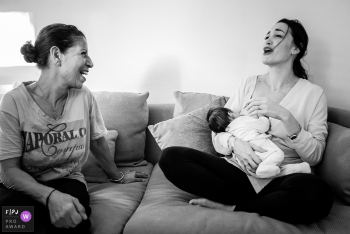 A mother breast feeds her baby as she and another woman have a conversation in this documentary-style family image recorded by a Landes photographer. 